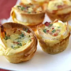 Petits quiches wraps dorés, garnis d'œufs, de lardons et de persil, servis sur une assiette blanche.