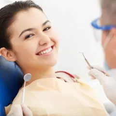 Uśmiechnięta pacjentka na fotelu dentystycznym, podczas gdy dentysta przygotowuje się do zabiegu z użyciem materiału glasjonomer.