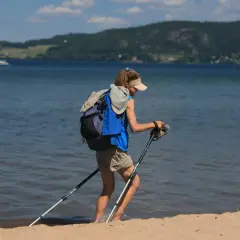 Osoba z plecakiem i kijkami do nordic walking nad morzem, wchodząca do wody.