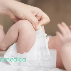 Dłoń poprawia pieluszkę niemowlęciu, zapobiegając pieluszkowemu zapaleniu skóry.
