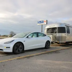 Une voiture électrique blanche tracte une caravane Airstream argentée. La question "peut on tracter avec une voiture electrique" trouve ici une réponse visuelle.