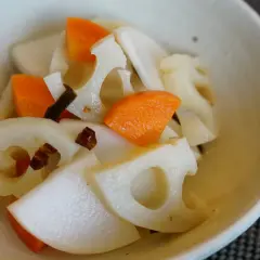 A close-up of a bowl filled with a colorful mix of Japanese root vegetables, including sliced lotus root with its distinctive holes, bright orange carrot pieces, and possibly daikon radish.