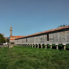 El horreo de Carnota, una estructura de piedra sobre pilares, se alza majestuoso ante una iglesia y un cielo azul.
