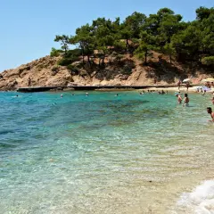 Słoneczna plaża na Thassos, z turkusową wodą i skalistym wybrzeżem. Ludzie kąpią się i odpoczywają, ciesząc się urokami wyspy. To idealne miejsce na wakacje, pełne atrakcji.