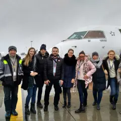 Grupa osób pozuje przed samolotem Bombardier Q400, z logo IATA na kadłubie.