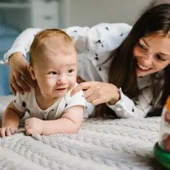 Mamma incoraggia il suo neonato di 1 mese in una divertente attività sul lettone, con un giocattolo colorato.