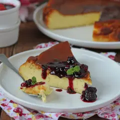 Una fetta di cheesecake basca cremosa, con topping di frutti di bosco e menta, su un piatto bianco.