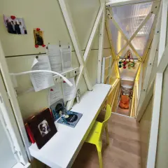 Wnętrze domku, biurko z książkami i zdjęciami, schody prowadzące do pomarańczowego fotela.