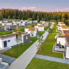 Reihe von kleinen Häusern, modern und minimalistisch, mit begrünten Dächern, eingebettet in eine grüne Landschaft am Waldrand.