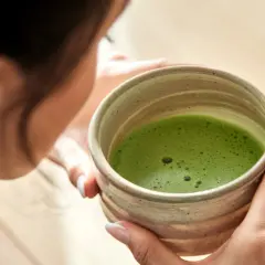 Frau hält eine Schale mit schaumigem, leuchtend grünem Matcha. Die ideale matcha temperatur für den perfekten Genuss.