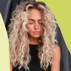 Mujer con cabello rubio, rizado y esponjoso, con los ojos cerrados y un ligero bronceado.