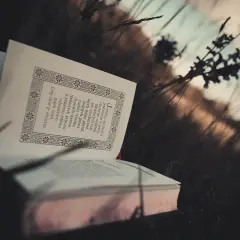 Otwarta księga pośród traw, jej strony zdobią ozdobne ramki i tekst. To chwila zadumy, modlitwa uwielbienia w naturze.