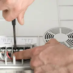 Ręce montują przewody do piekarnika. Wkrętarka dokręca śrubę przy zacisku, a palec wskazuje kolejny.