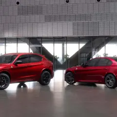 Dwa czerwone Alfa Romeo, SUV Stelvio i sedan Giulia Quadrifoglio, stoją obok siebie w nowoczesnym wnętrzu.