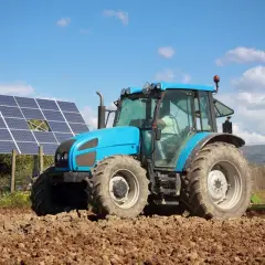 Błękitny traktor orze pole obok paneli fotowoltaicznych. Rolnik korzysta z dofinansowania dla rolników fotowoltaika, inwestując w zieloną energię.