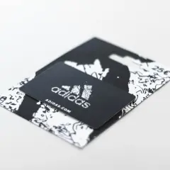 Czarny voucher Adidas z logo i adresem strony internetowej. Dowiedz się, jak zrobić voucher na prezent.