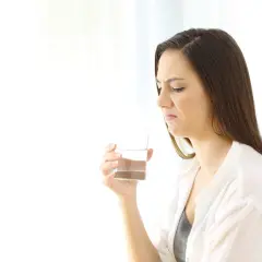 Donna con espressione disgustata tiene un bicchiere d'acqua, avvertendo un sapore metallico in bocca.