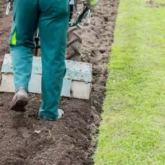 Osoba w zielonych spodniach używa glebogryzarki do przygotowania ziemi. To pierwszy krok, jak założyć trawnik.