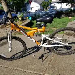An orange Mongoose XR-75 mountain bike with a black seat and white suspension sits on a sidewalk.