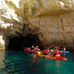 Kayakistas exploran las impresionantes cuevas de Cabo de Gata, navegando por aguas cristalinas bajo acantilados dorados.