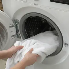 Ręce wkładają biały ręcznik do pralki. Zastanawiasz się, co najlepiej przywraca biel ubraniom? Pranie to klucz.
