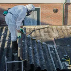 Pracownik w kombinezonie ochronnym usuwa eternit z dachu, dbając o bezpieczeństwo przy pracy z materiałem zawierającym azbest.