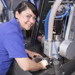 Frau mit blauen Polohemd arbeitet an einer CNC-Maschine. Sie vertieft sich in ihre Weiterbildung als Zerspanungsmechanikerin.