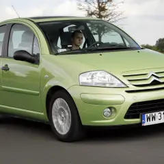 Zielony Citroen C3 2005 z młodym kierowcą za kierownicą przemierza wiejską drogę.