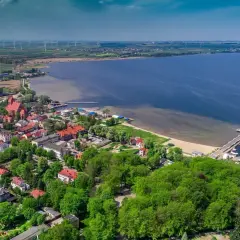 Widok z lotu ptaka na miasto nad Zatoką Pucką, z portem jachtowym, plażą i wiatrakami na horyzoncie.