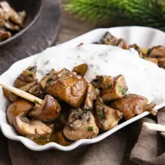 Gebratene Champignons mit Kräuterquark, wie vom Weihnachtsmarkt, auf einem weißen Teller mit Holzspießen.