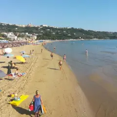 Plage animée à Vasto, Italie, avec des parasols colorés, des baigneurs et une ville en arrière-plan.