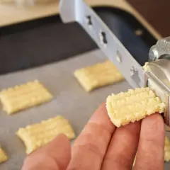 Ręka trzyma świeżo wyciśnięte ciastka z maszynki, gotowe do pieczenia.