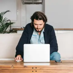 Mężczyzna siedzi na kanapie, pracując na laptopie. Wpisuje swój adres rozliczeniowy, aby dokończyć zamówienie.