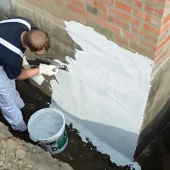 Mann dichtet die Wand mit Spachtel und Mörtel ab. Ein Eimer mit Material steht bereit.