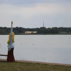 Drewniane figury nad jeziorem w Nowym Warpnie. Dziecko z lornetką i kobieta z podniesioną ręką patrzą na wodę.