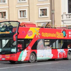 Un bus rouge à deux étages, un bus touristique "City Sightseeing Roma", circule dans la ville.