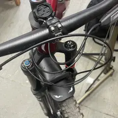 Close-up of a mountain bike's handlebars and front fork, showing the brake levers and the neat routing of the cutting hydraulic hose.