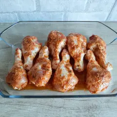 Osiem pałek z kurczaka w szklanej brytfannie, gotowych do pieczenia.
