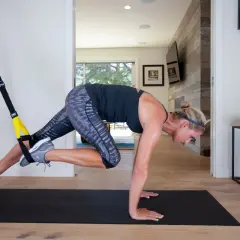 Kobieta wykonuje ćwiczenie z taśmami TRX, angażując mięśnie brzucha i nóg. Intensywny trening TRX w domowym zaciszu.