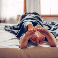 Zwei Füße berühren sich unter einer Decke. Ein Paar, das sich an die Regel "kein Sex vor der Ehe" hält, genießt die Nähe.