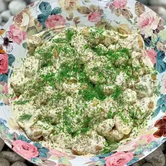 En stor skål med krämig potatissallad, toppad med dill och gräslök. Den vackra skålen har ett blommönster med fjärilar. Detta är nog den godaste potatissalladen!