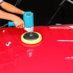 Mani che usano una lucidatrice blu per lucidare la macchina rossa, ottenendo una finitura brillante.