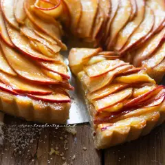 Una deliziosa crostata di mele, con le fette di mela disposte a rosa e lucide di glassa, su un tagliere di legno.