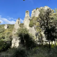 Les Aiguilles de Valbelle, formations rocheuses spectaculaires, se dressent sous un ciel bleu, entourées de verdure.