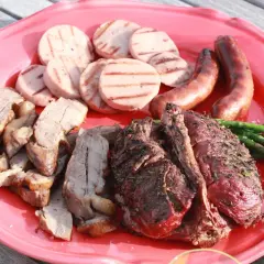 En stor röd bricka med grillad rådjur, korv, grillad korv och sparris. En härlig sommarmåltid!