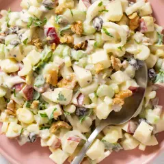Ensalada Waldorf cremosa con trozos de manzana, apio, nueces y pasas, servida en un plato rosa.