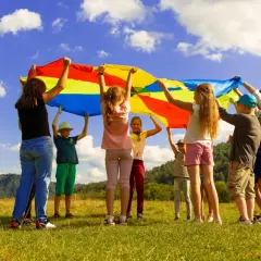 Dzieci trzymają kolorową chustę animacyjną na tle nieba i gór.