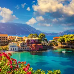 Piękna kefalonia pogoda czerwiec: kolorowe domki nad turkusową zatoką, góry w tle, kwitnące kwiaty na pierwszym planie.