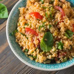 Una ciotola di insalata di cous cous con pomodorini e erbe fresche, pronta per essere gustata.