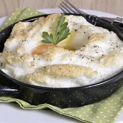 Delicioso huevo al horno, con clara montada y yema cremosa, adornado con perejil y pimienta.